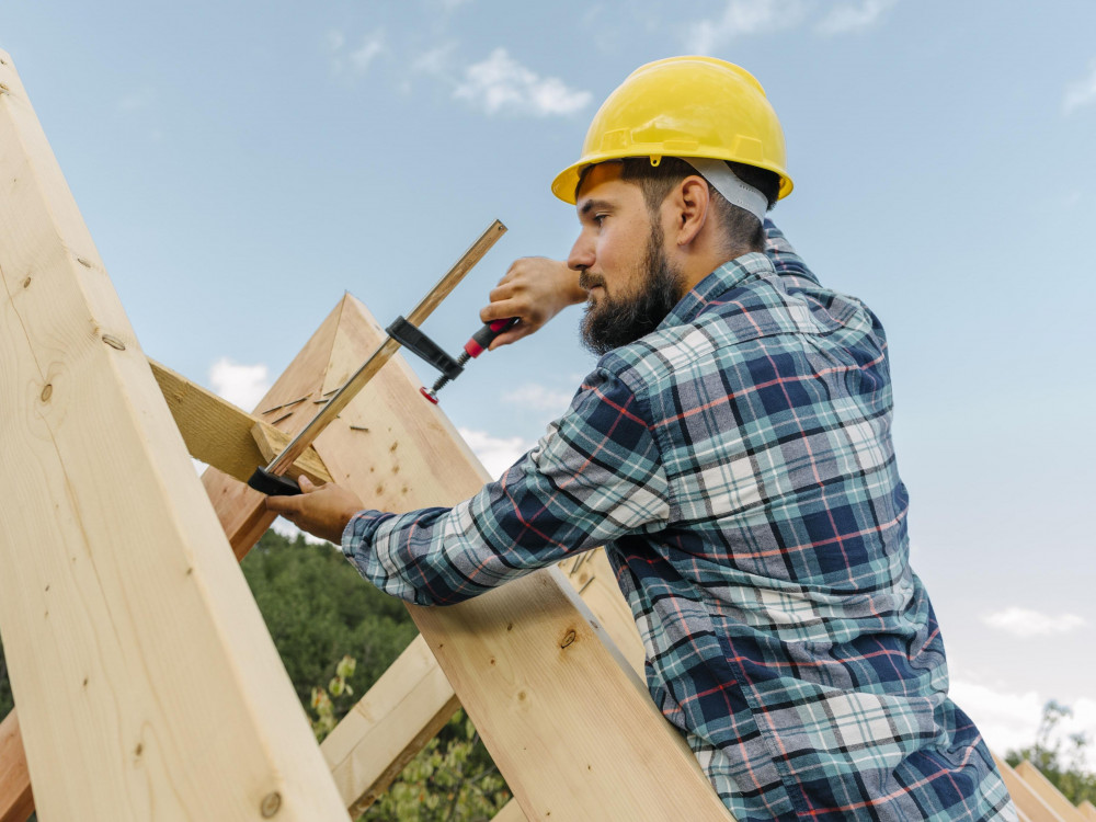 Zimmerer bei der Arbeit am Dachstuhl aus Holz Handwerker mit Schutzhelm befestigt Holzbalken beim Bau eines Dachstuhls