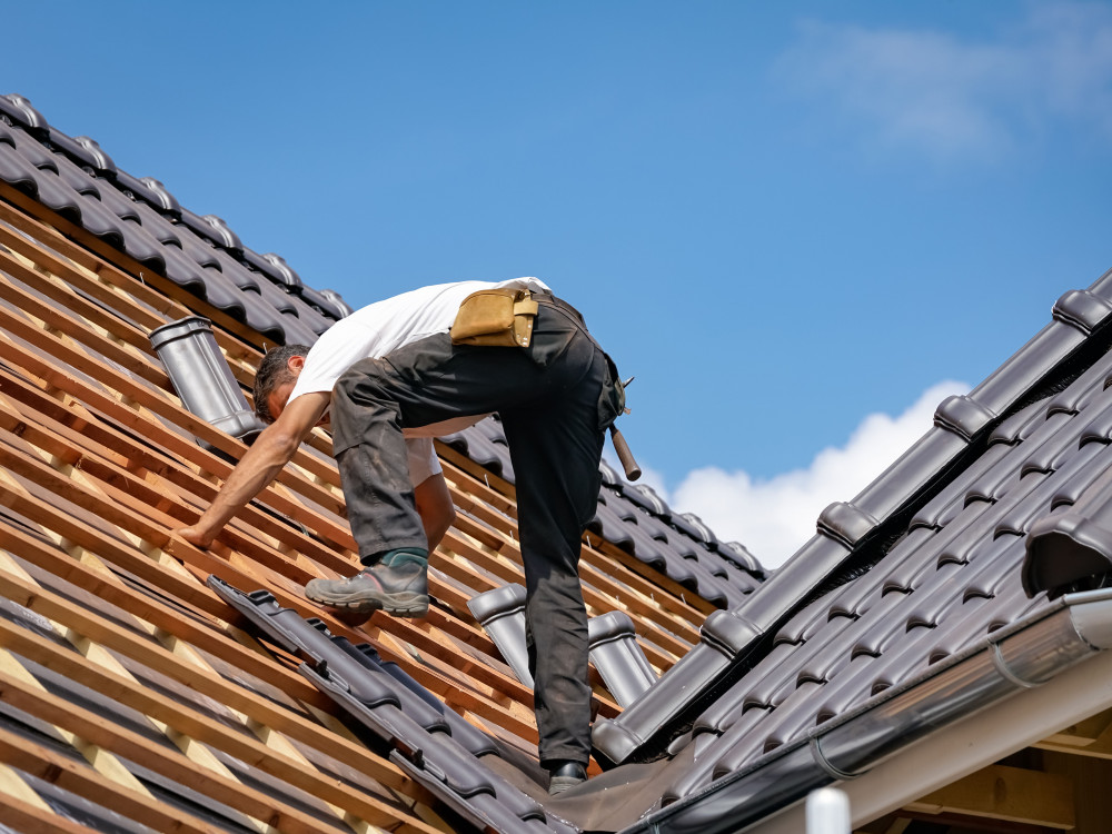 Dachdecker bei der Eindeckung eines Steildachs mit Ziegeln Handwerker arbeitet auf dem Dach und verlegt Dachziegel bei der Neueindeckung