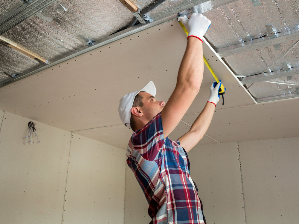 Handwerker beim Trockenbau und Deckenmontage mit Gipskartonplatten Bauarbeiter misst Metallkonstruktion für Trockenbaudecke mit Dämmung und Gipskarton